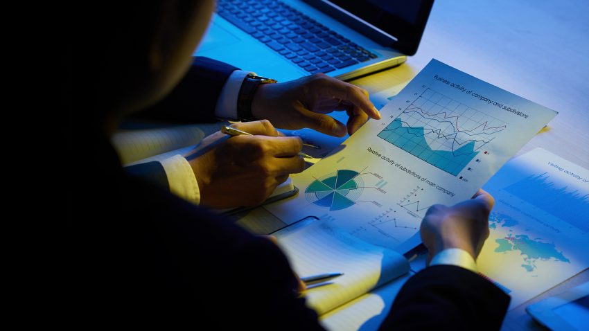 Two businesspeople analyze charts and graphs over a desk with a laptop in the background.
