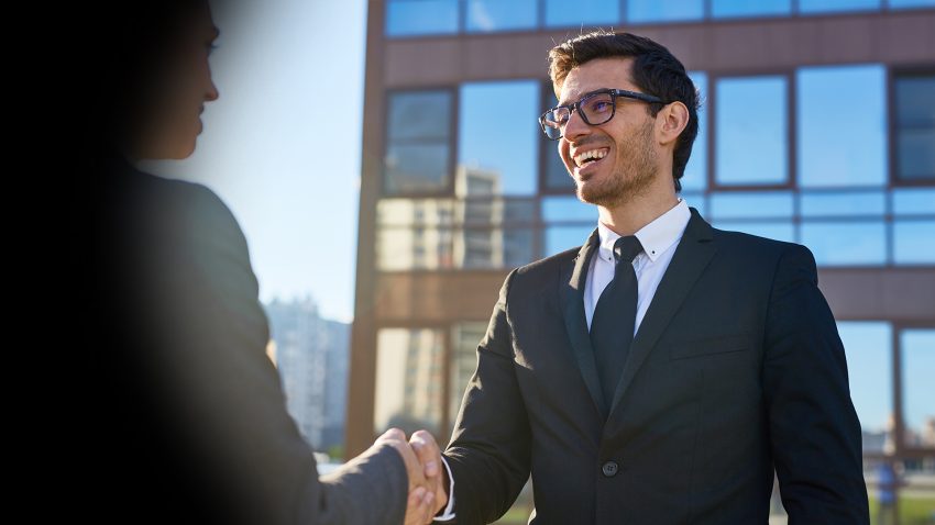 Business professionals shaking hands to discuss AI and cloud transformation with a Microsoft partner.
