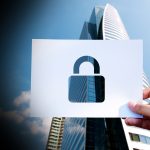 Hand holding a white card with a cutout padlock symbol, symbolizing security against a cityscape background.