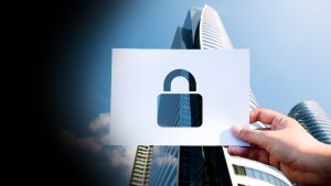 Hand holding a white card with a cutout padlock symbol, symbolizing security against a cityscape background.