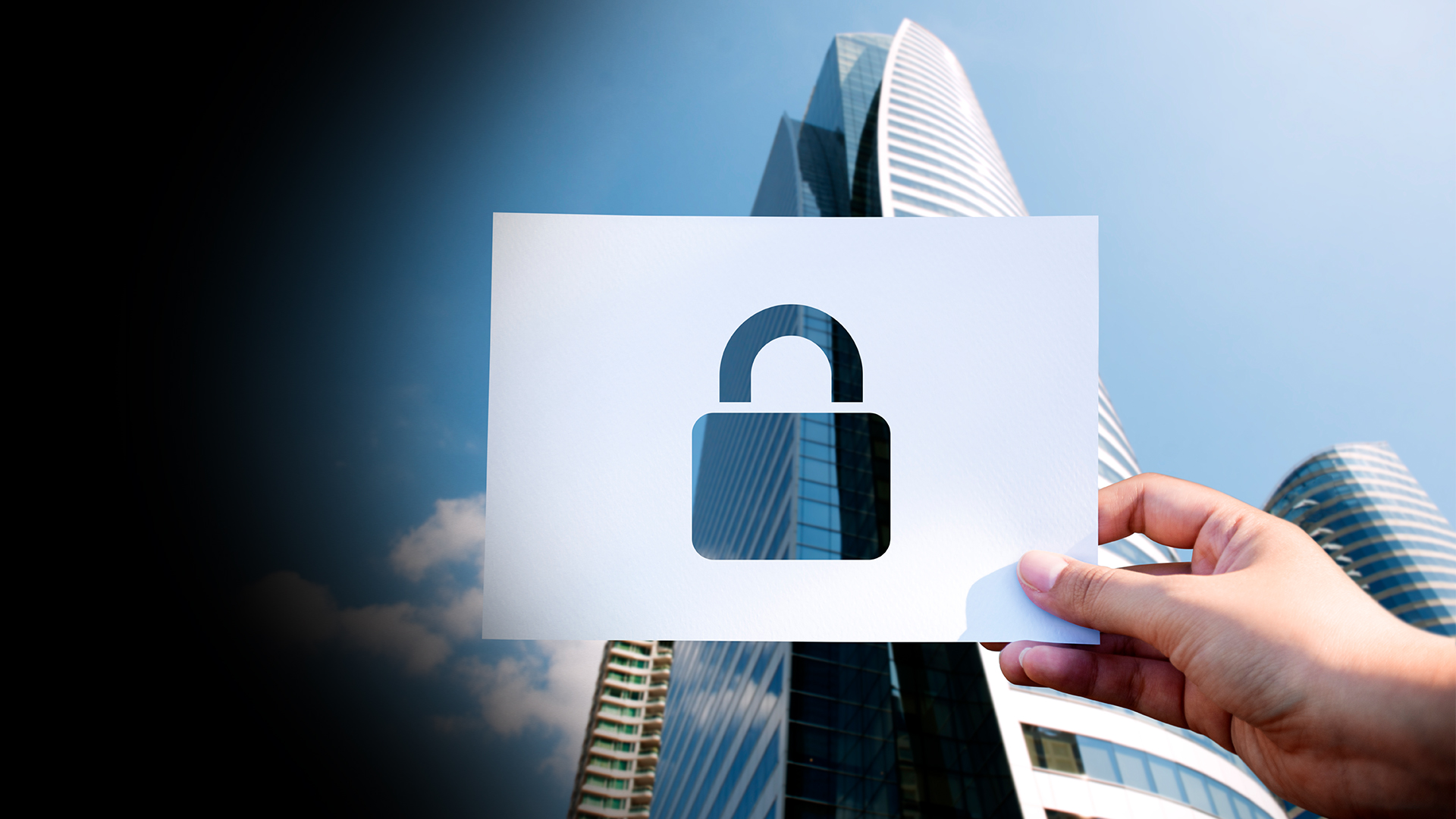 Hand holding a white card with a cutout padlock symbol, symbolizing security against a cityscape background.